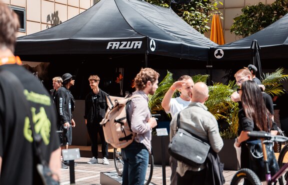 You can see a black 8x4 m gazebo with three roof flags. The flags and the roof of the gazebo are printed with the customer's white logo. Many people can be seen in the foreground.