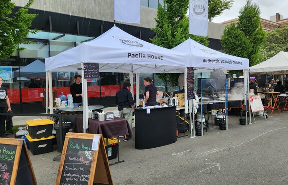 Two white folding gazebos stand at a market. They both have printed roofs and one printed flag each.