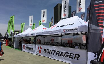 Mehrere weiße Promotionszelte mit dem Logo "Bontrager" überdachen Fahrräder und zwei Mitarbeiter der Firma.