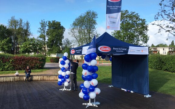 Ein blauer Faltpavillon der Firma "Barilla" ist mit weißen und blauen Luftballons geschmückt, die von einem Mann angebracht werden.