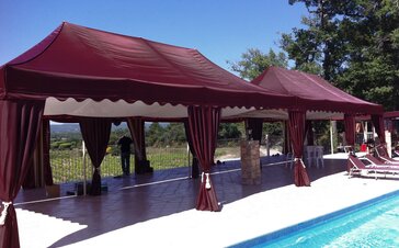 Zwei weinrote Falpavillons  in eleganter Ausführung stehen nebeneinander an einem Pool und schützen die Gäste vor der Sonne.
