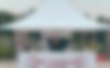 Auf dem Bild ist ein weißer Faltpavillon zu sehen, der als Street Food-Stand dient. Die vordere Seitenwand auf halber Höhe ist mit dem roten Firmenlogo bedruckt. Unter dem Zelt befinden sich ein Pizzaofen und der Pizzabäcker.
