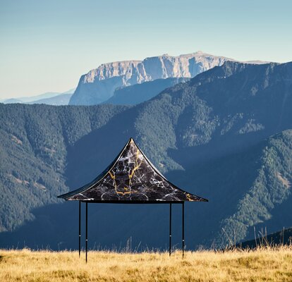 Gazebo pieghevole nero con 4 tettoie e stampa individuale sulla montagna Plose. Dietro si vede la catena montuosa.