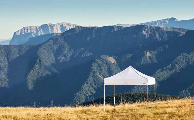 White gazebos on the Plose mountain. In the background there is a mountain range called Dolomites. 