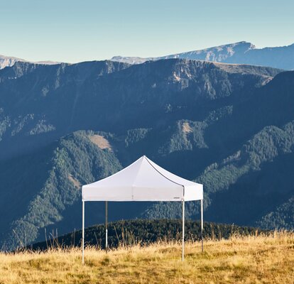 White gazebos on the Plose mountain. In the background there is a mountain range called Dolomites. 