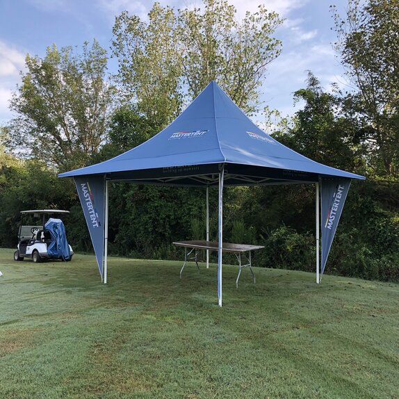 Gazebo pieghevole blu con tettoie e bandiere angolari si trova su un prato in un campo da golf. Il gazebo è personalizzato con il logo MASTERTENT.