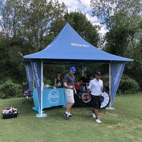 Due giocatori di golf bevono qualcosa al gazebo pieghevole blu con tettoie e bandiere angolari