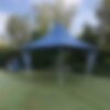 Ein blauer Faltpavillon mit Vordach und vier Eckfahnen steht auf der Wiese eines Golfplatzes. Das MASTERTENT-Logo ist sowohl auf den Dachschrägen als auch auf den Eckfahnen aufgedruckt.