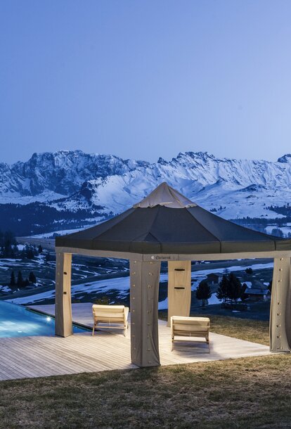 Das Lodenzelt steht auf der Terrasse neben dem Pool. Dahinter strahlen die Berge im Abendlicht.