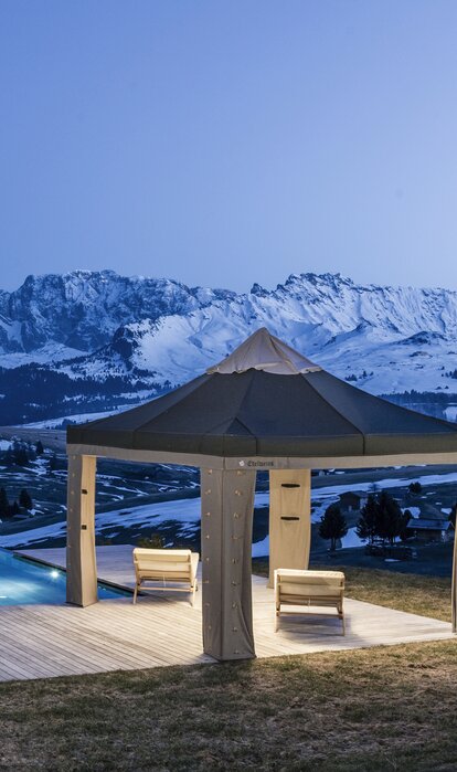 Das Lodenzelt steht auf der Terrasse neben dem Pool. Dahinter strahlen die Berge im Abendlicht.