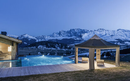 Das Lodenzelt steht auf der Terrasse neben dem Pool. Dahinter strahlen die Berge im Abendlicht.
