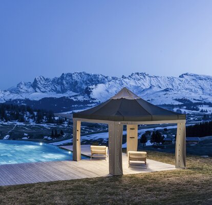 The loden tent is located on the terrace next to the pool. In the background the mountains are glowing in the evening light. 