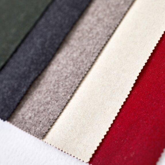 The five fabrics of the loden tent are lying next to each other: green, dark grey, light grey, beige, red. 