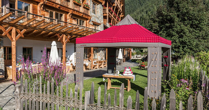 Rot-graues Lodenzelt steht im Garten einer Gaststätte; unter dem Faltpavillon befindet sich ein Tisch mit Sektgläsern und Torte.