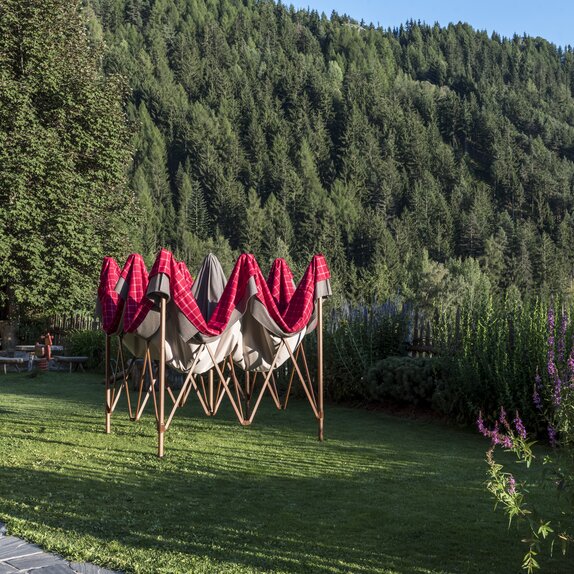 Leicht aufgezogener Faltpavillon mit rot-grauem Lodenstoff-Überzug im Garten.