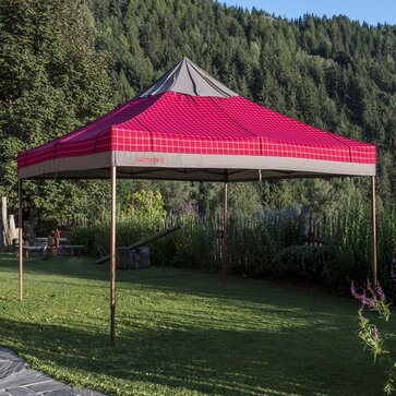 The gazebo with the red-grey loden fabric cover has been fully opened. It is placed in the garden. 