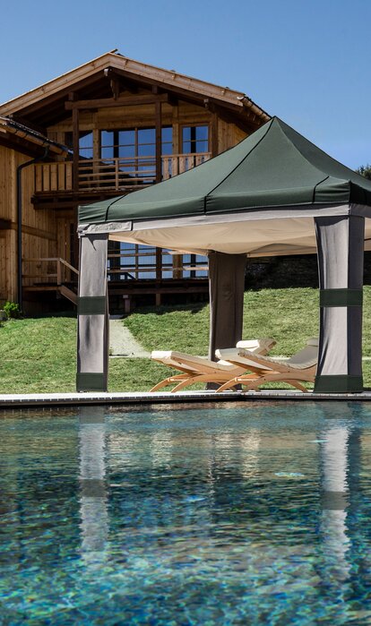 Vicino la piscina c'è un gazebo pieghevole Loden con cielo. Sotto il gazebo pieghevole Loden ci sono due sdrai.