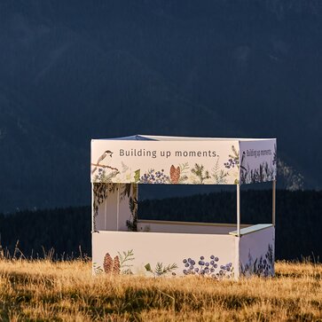 The gazebo with flat roof - Square - is located at the Plose mountain at the sunset. The gazebo is white and printed. 
