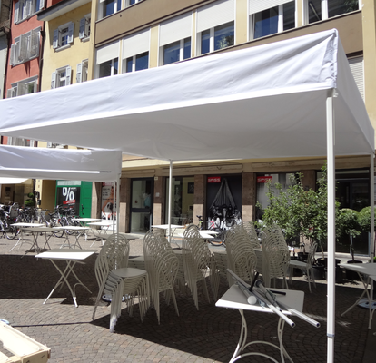 Gazebo pieghevole bianco con tetto piano su misura 4x4m davanti ad un bar. Sotto si trovano tavoli e panche.