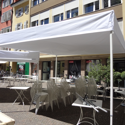 Gazebo pieghevole bianco con tetto piano su misura 4x4m davanti ad un bar. Sotto si trovano tavoli e panche.