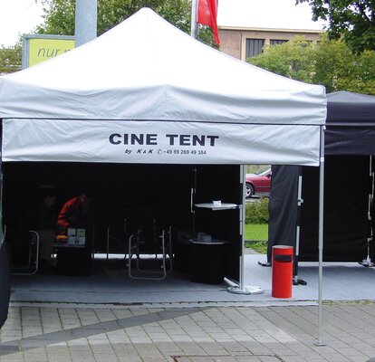 Il gazebo pieghevole appositamente progettato è dotato di un banner pubblicitario stampato "CINE TENT" rimovibile. Questo è attaccato al frontalino del tetto e ai montanti d'angolo del gazebo pieghevole con un velcro come una parete laterale.