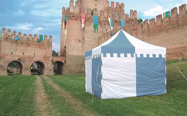 A custom made gazebo in the colours blue and white is standing in the meadow in front of a castle. The valance of the roof reminds at a castle. 