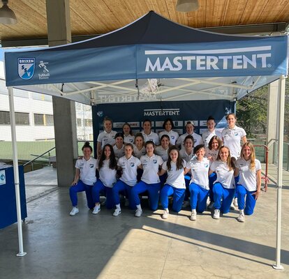 Una squadra di calcio femminile si trova sotto un gazebo pieghevole con un tetto blu.