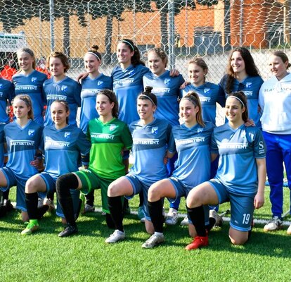 Su un campo da calcio, sotto una porta, le calciatrici di una società sportiva altoatesina sono in piedi o in ginocchio.