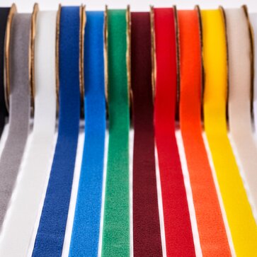 Rollen der Klettstreifen liegen in allen Farben nebeneinander: schwarz, grau, hellgrau, dunkelblau, hellblau, grün, bordeaux, rot, orange, gelb, ecru, weiß.