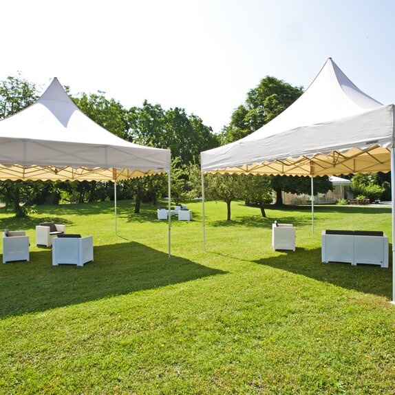 Gazebo pieghevoli color crema con tetto a pagoda con frontalino ondulato in un giardino per lounge evento all'aperto