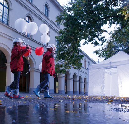 2 children with balloons are passing by the illuminated gazebo. 
