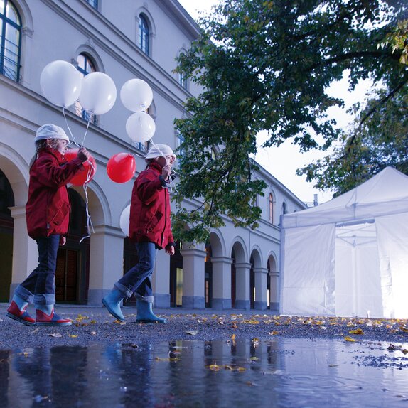 2 children with balloons are passing by the illuminated gazebo. 