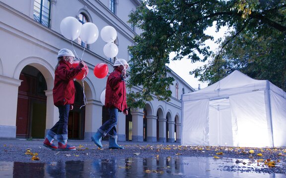 2 children with balloons are passing by the illuminated gazebo. 