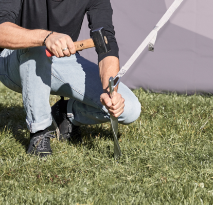 Befestigung eines Faltpavillons mit Hering und Hammer auf einer Wiese