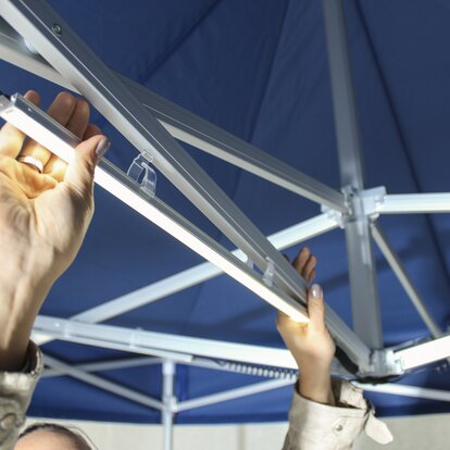 Installing LED light strips on the roof of a blue Mastertent folding gazebo