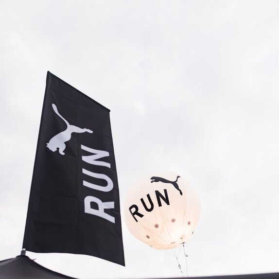 A black peak flag printed with a white Puma logo on top of a Mastertent canopy tent.