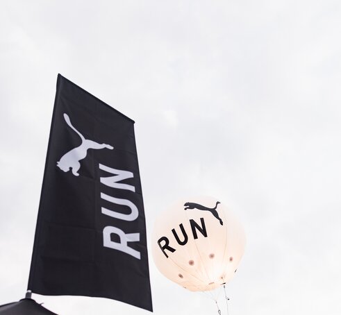 A black peak flag printed with a white Puma logo on top of a Mastertent canopy tent.
