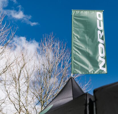 A green peak flag printed with the NORCO logo on top of a canopy tent.