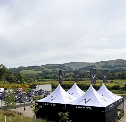 A 2x2 set up of 17x17 Mastertent Canopy Tents with peak flags and walls next to a line of smaller 10x10ft canopy tents set out in a large spacious area.