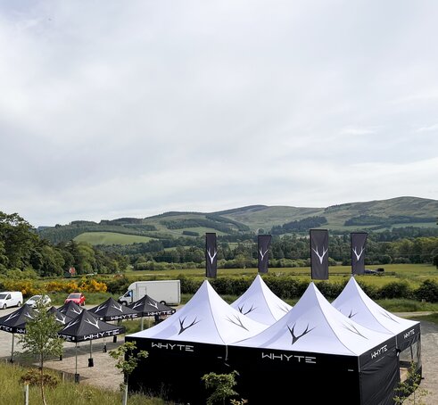A 2x2 set up of 17x17 Mastertent Canopy Tents with peak flags and walls next to a line of smaller 10x10ft canopy tents set out in a large spacious area.