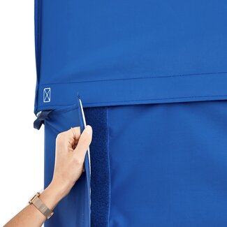 A woman is attaching the blue sidewall to the blue gazebo with a full-lenght velcro strip. 