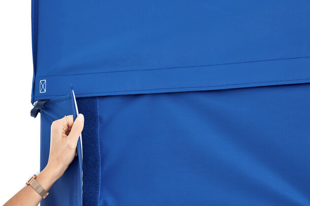 A woman is attaching the blue sidewall to the blue gazebo with a full-lenght velcro strip. 