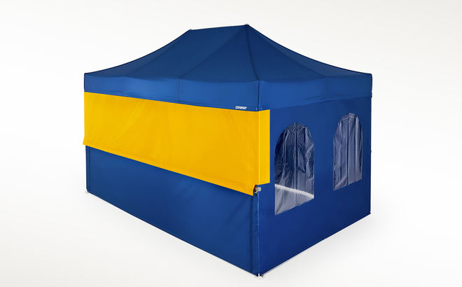 A Mastertent with blue roof and sidewalls with a yellow upper closure wall to fully enclose a half-height wall.