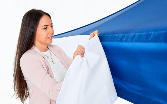 Woman is attaching an exchangeable valance to the panel of the gazebo. It is attached by velcro strips. 